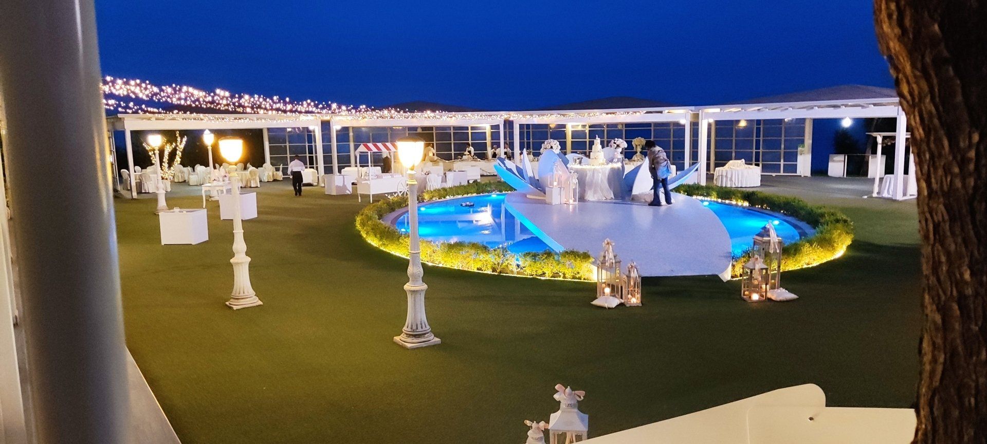 Una grande piscina è circondata da tavoli e sedie durante un ricevimento di nozze.