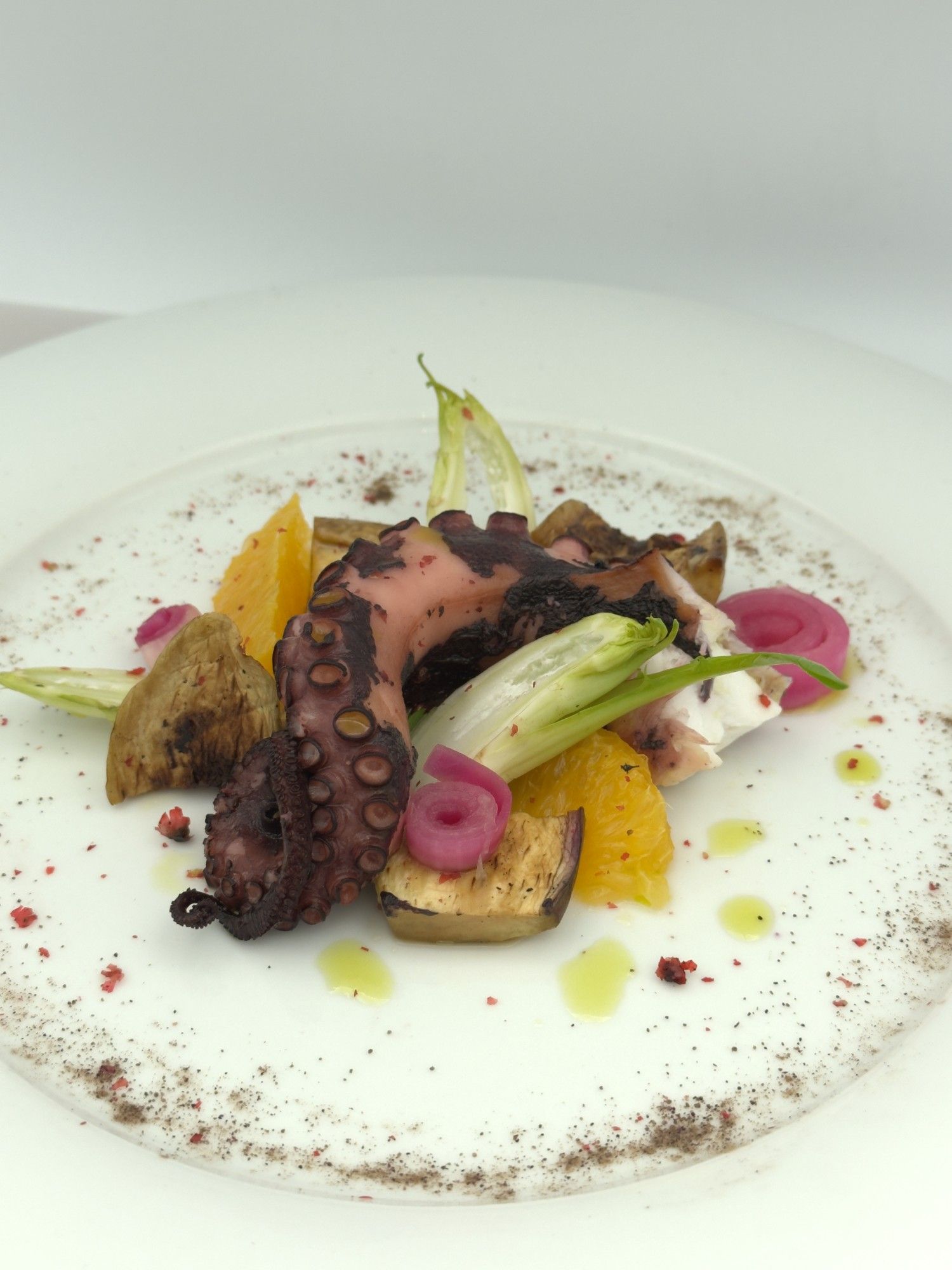 Un piatto bianco con sopra polpo e verdure
