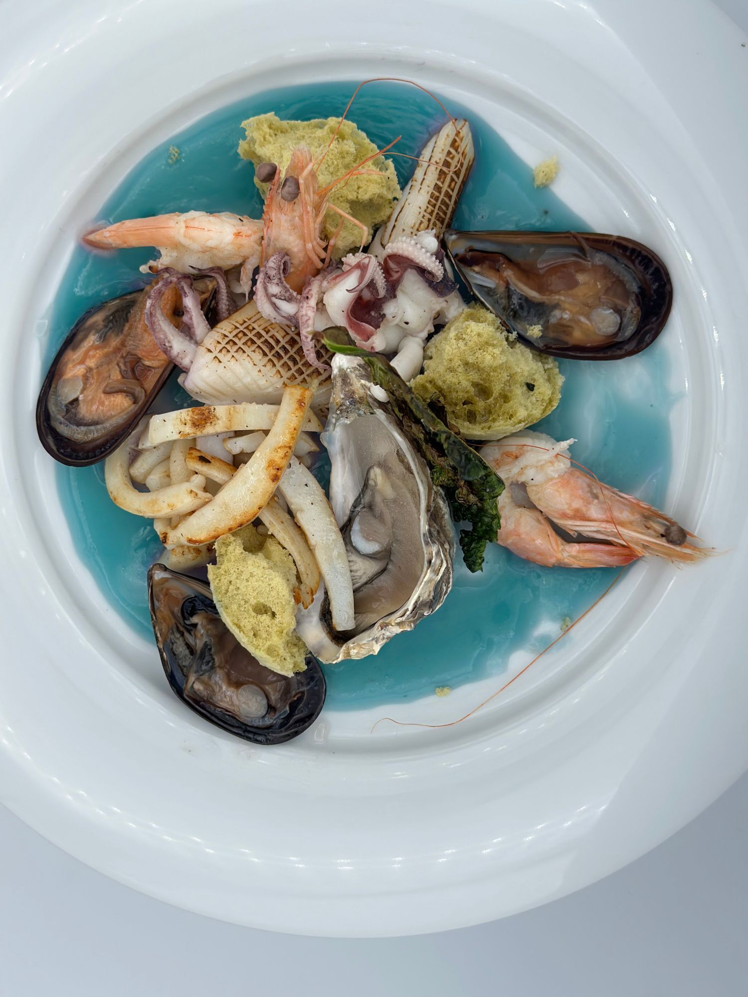Un piatto bianco guarnito con frutti di mare e salsa blu.