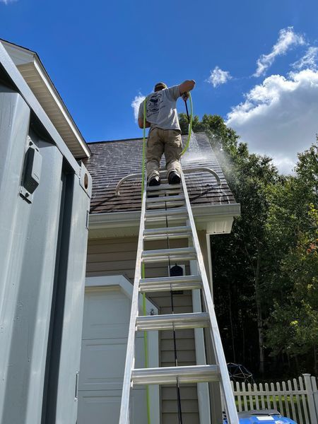 Person pressure washing a roof from a ladder on a sunny day.