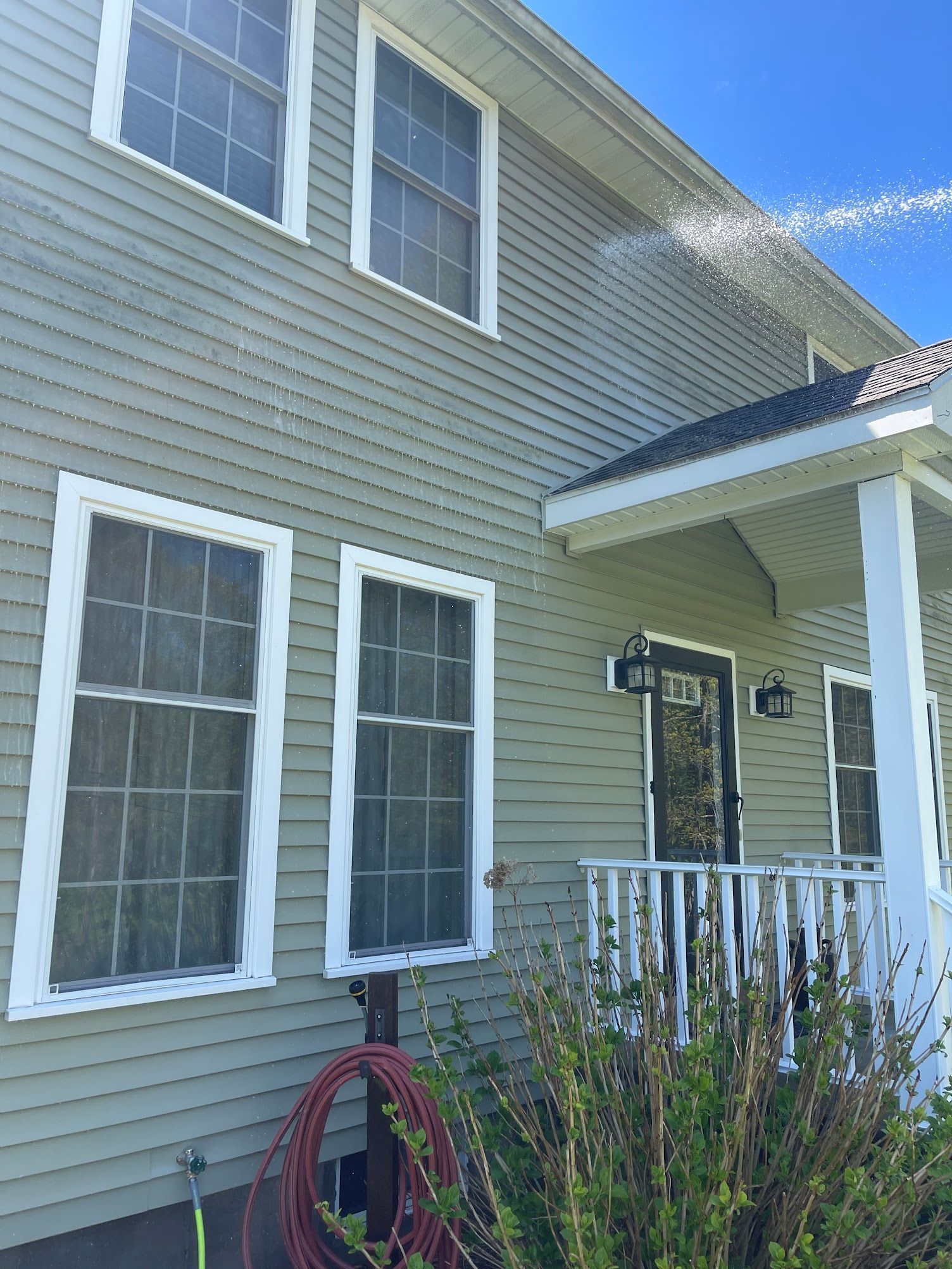 Two-story house with green siding being pressure washed; white trim, porch, windows, blue sky.