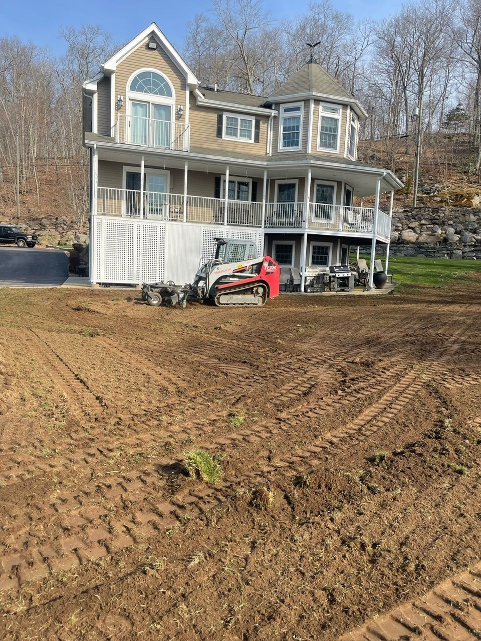House with multiple levels and wraparound balconies, a small construction vehicle in yard. Earthwork in progress.