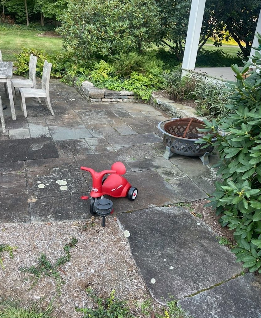 Red tricycle on a stone patio with a fire pit and outdoor furniture.