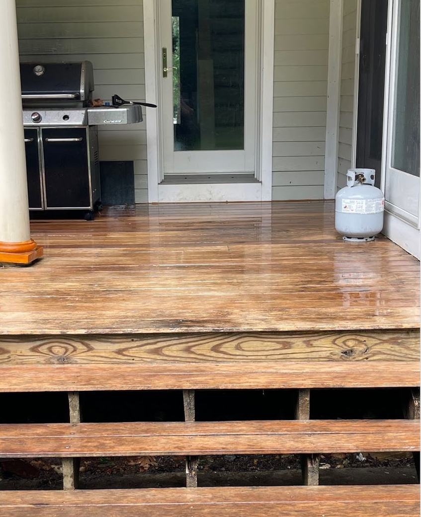 Wooden porch with grill, propane tank, and door. Steps are missing boards.
