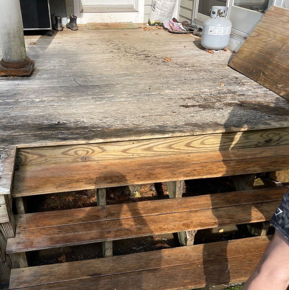 Wooden deck with steps, some boards missing. Gray weathered wood, sunlight.