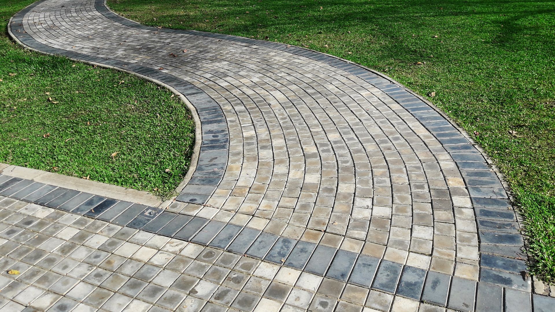 A brick walkway going through a lush green field.