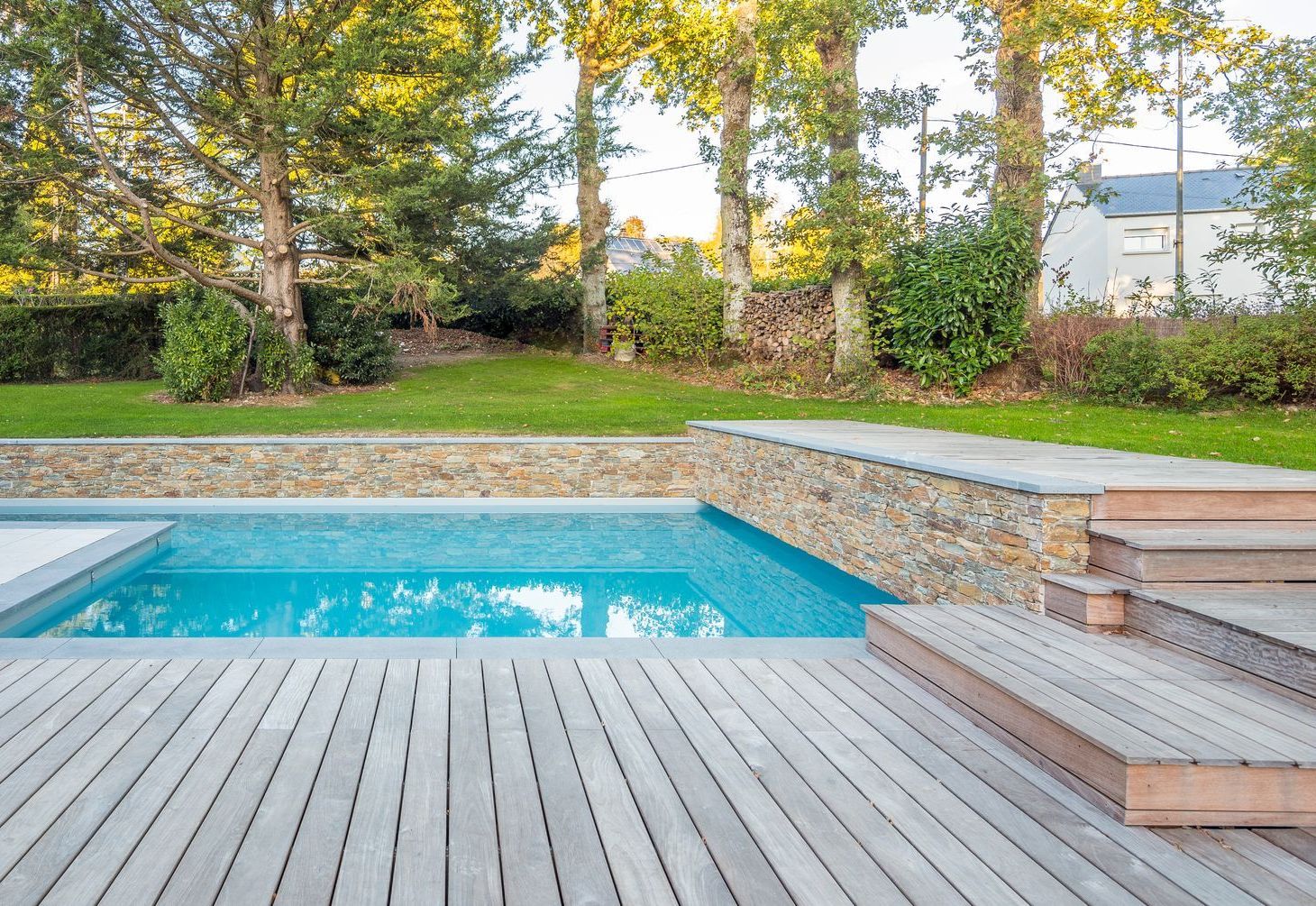 A large swimming pool is surrounded by a wooden deck in a backyard.