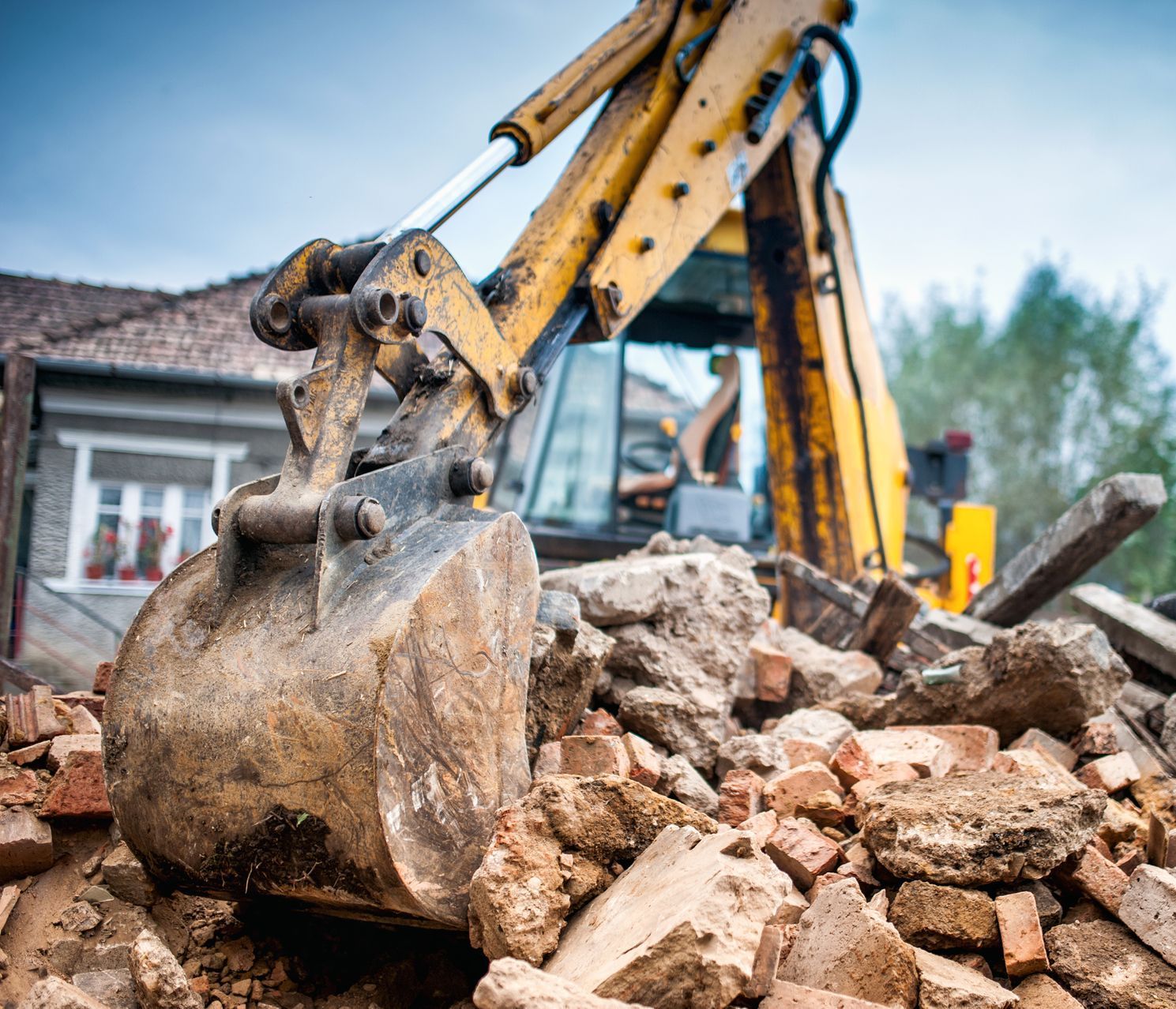 A bulldozer is demolishing a building with a pile of bricks in the foreground.