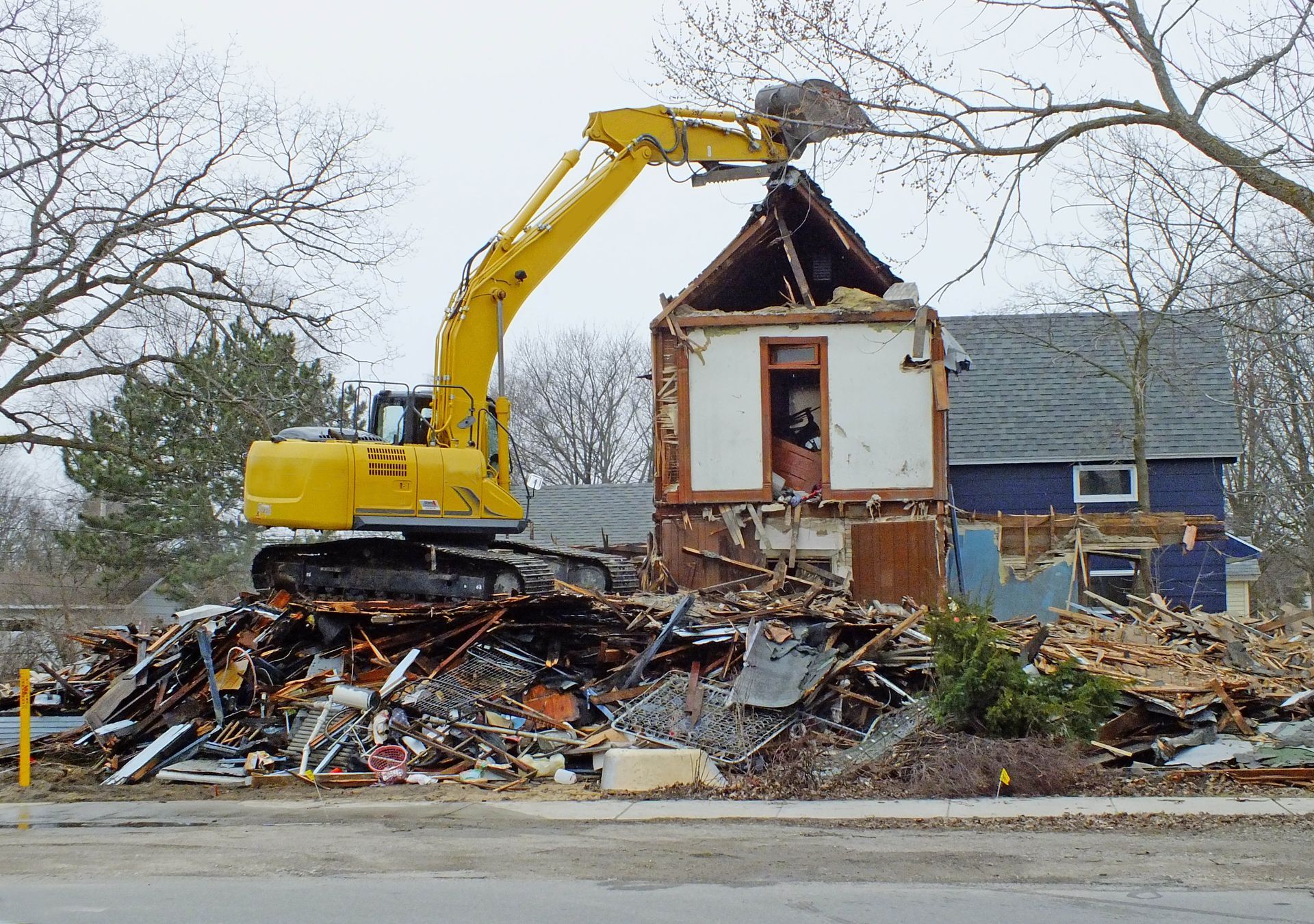 A large yellow excavator is demolishing a house