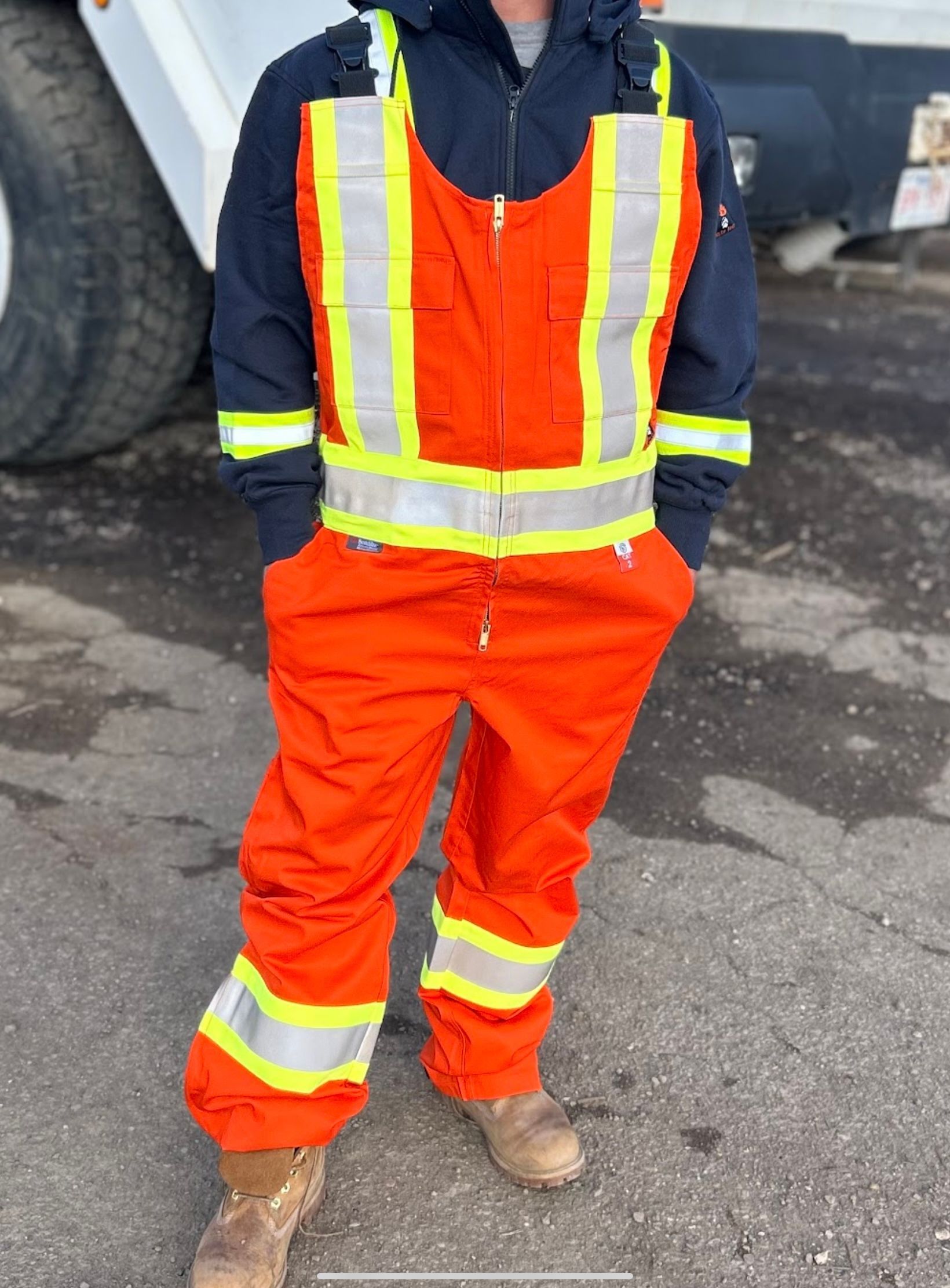 Person wearing black overalls with reflective yellow stripes, standing outdoors.