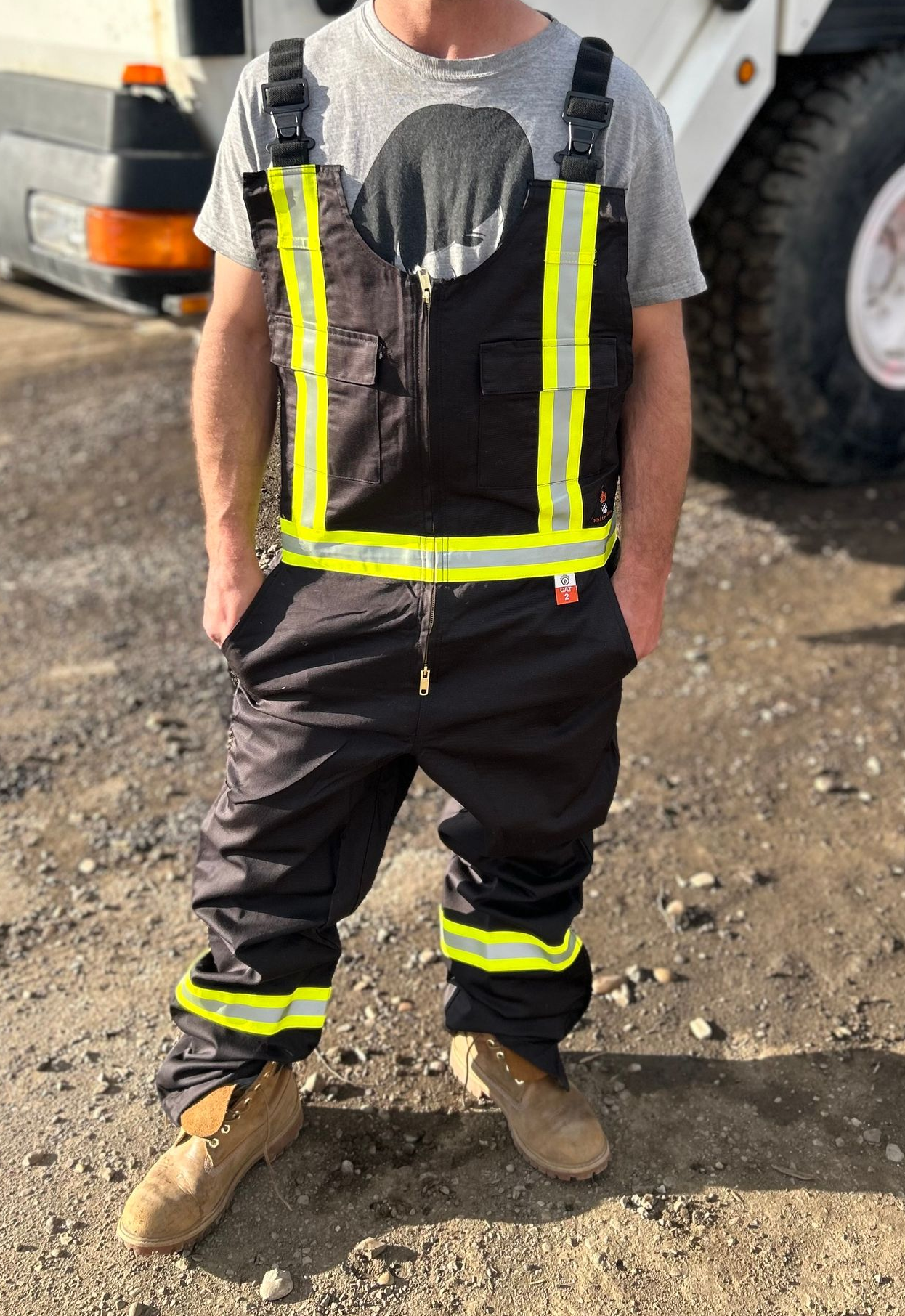 Person wearing black overalls with reflective yellow stripes, standing outdoors.