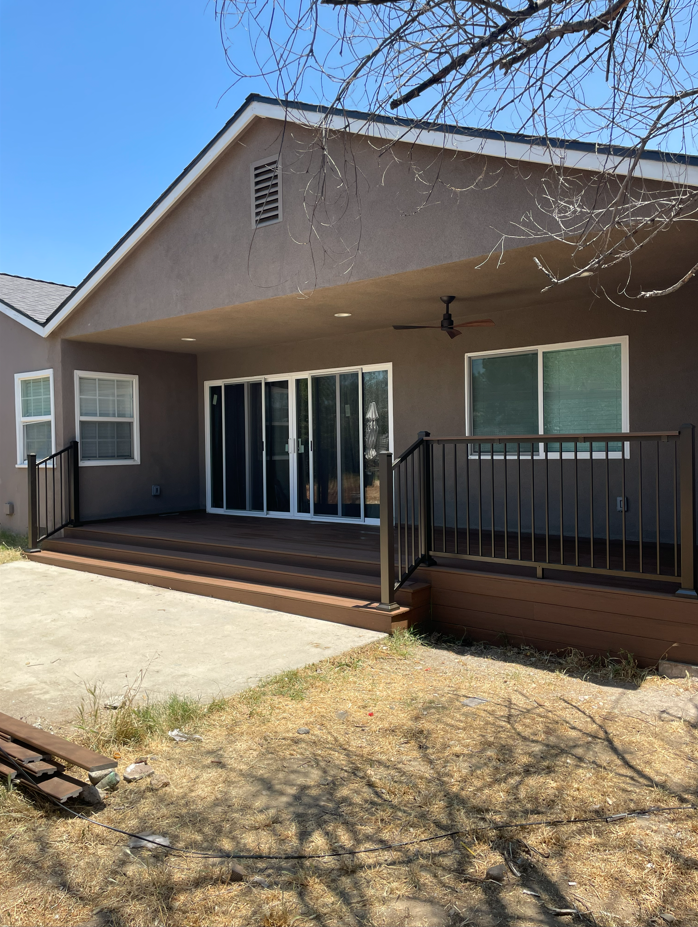 Backyard with brown deck, patio, and brown stucco house; sliding glass doors and windows.