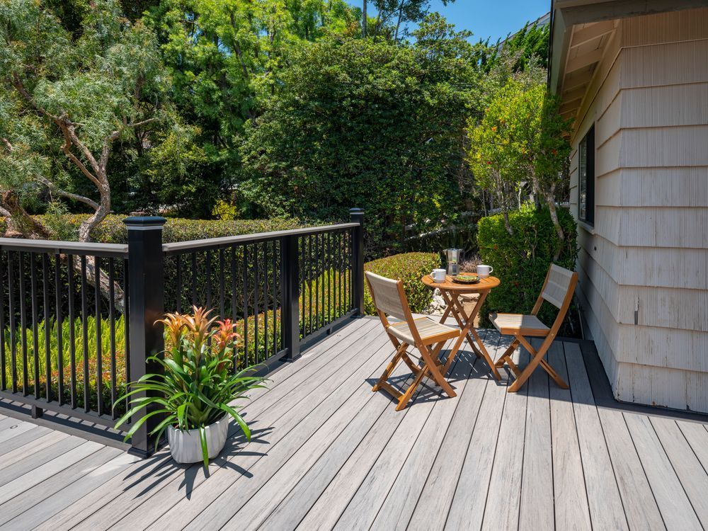 Wooden deck with table and chairs, potted plant, and green foliage.