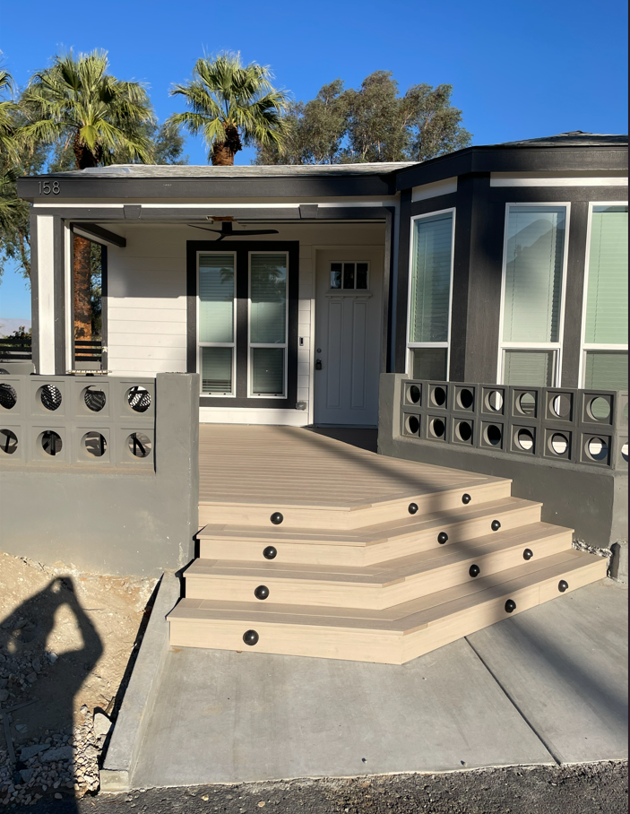 Modern house exterior with concrete steps and decorative wall, door, and windows. Palm trees in background.