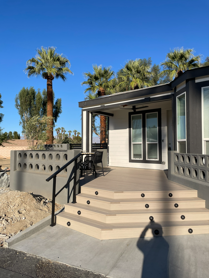 Exterior of a modern home with steps, black railing, and palm trees under a blue sky.