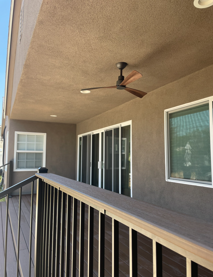 Deck with railing, ceiling fan, sliding glass doors, and windows, all under a brown-textured roof.