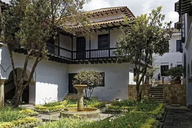 Courtyard with white buildings, trees, a fountain, and a dark wooden balcony in Bogotá, Colombia.