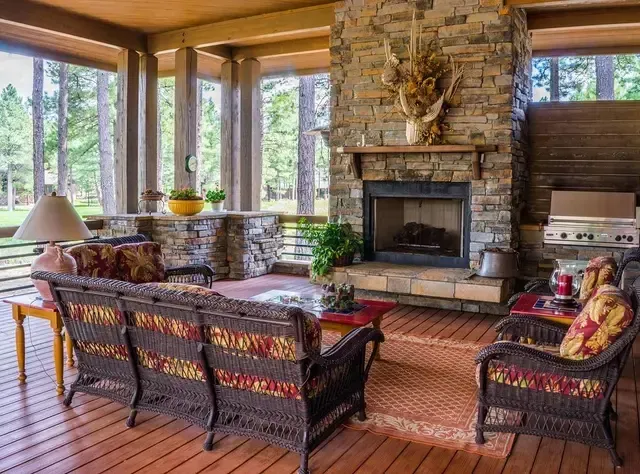 Outdoor living area with stone fireplace, wicker furniture, and forest view.