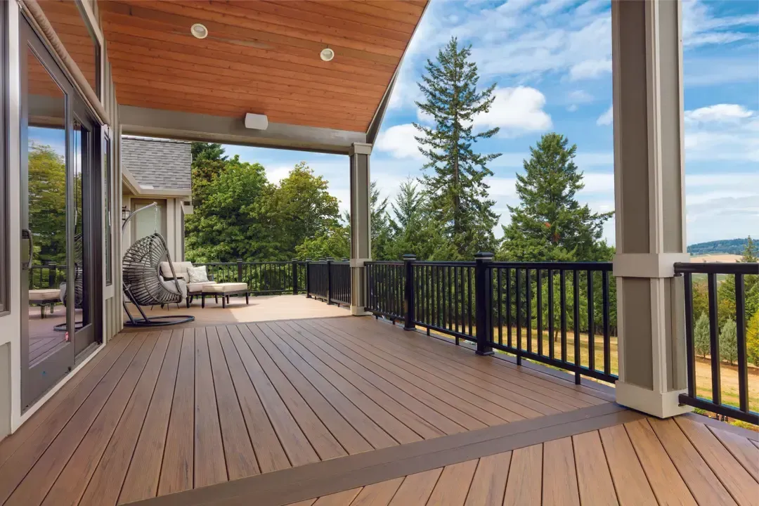 Wooden deck with black railing overlooking trees and blue sky.