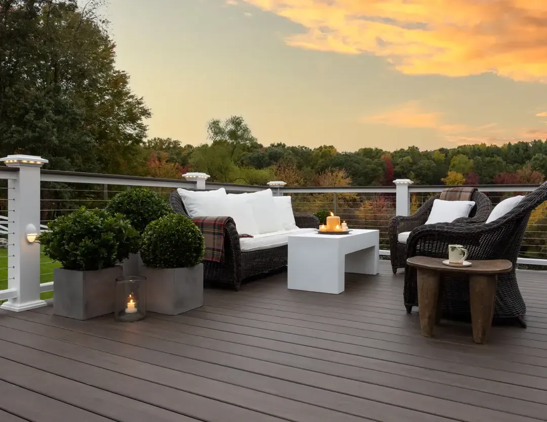 Outdoor deck with white furniture, potted plants, and candles; sunset view.