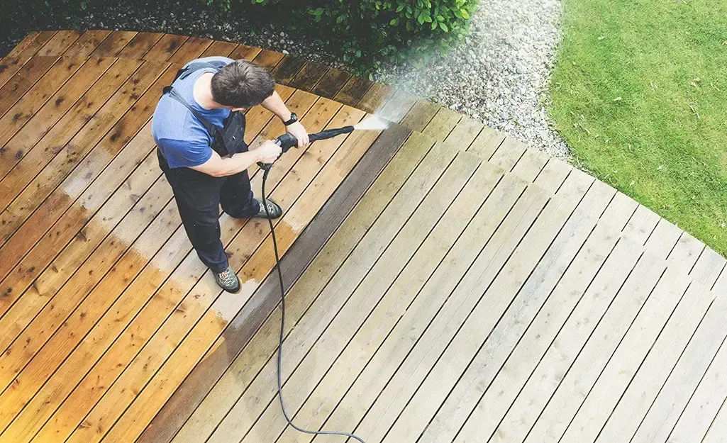 Person pressure washing a wooden deck, half clean, with water spray.