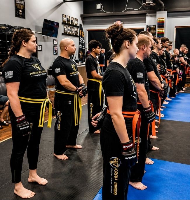 Five people in jiu-jitsu uniforms on a blue mat, including a man with a red belt, posing in a gym.