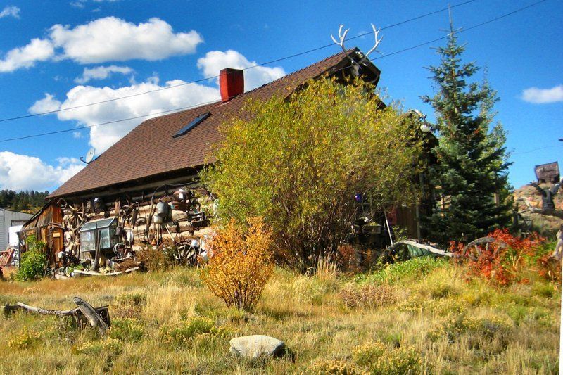 Rustic log cabin with antlers on roof, autumn foliage, and blue sky.