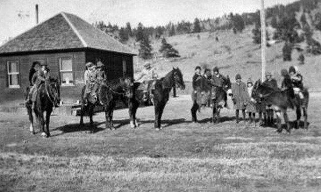Group of people on horseback, near a building. Some stand next to the horses.