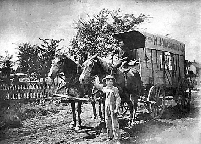 Horse-drawn wagon with two people inside, a boy standing in front. Wagon is labeled 
