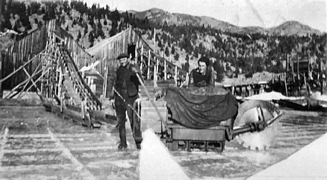 Two men harvesting ice blocks from a frozen lake with mountain backdrop.