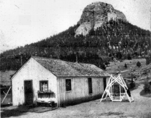 A small wooden building with a mountain in the background. A swing set sits to the right of the building.