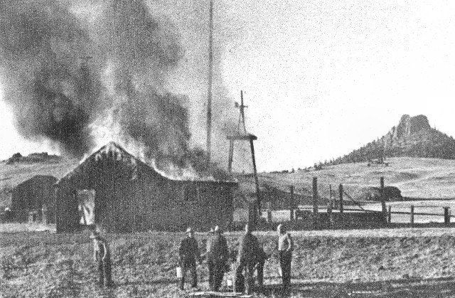 Building on fire with men watching; windmill nearby, mountain in background.
