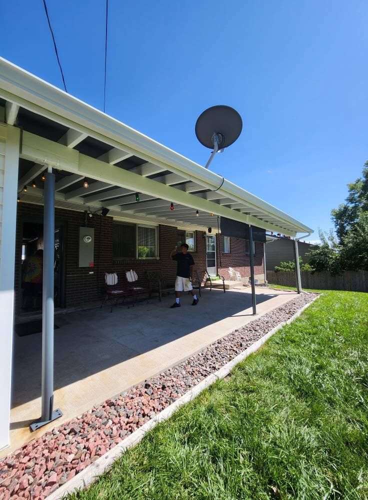 A man stands under a patio cover attached to a brick house on a sunny day.