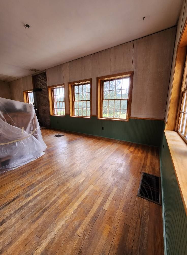 Empty room with wood floors, three windows, and green wainscoting.