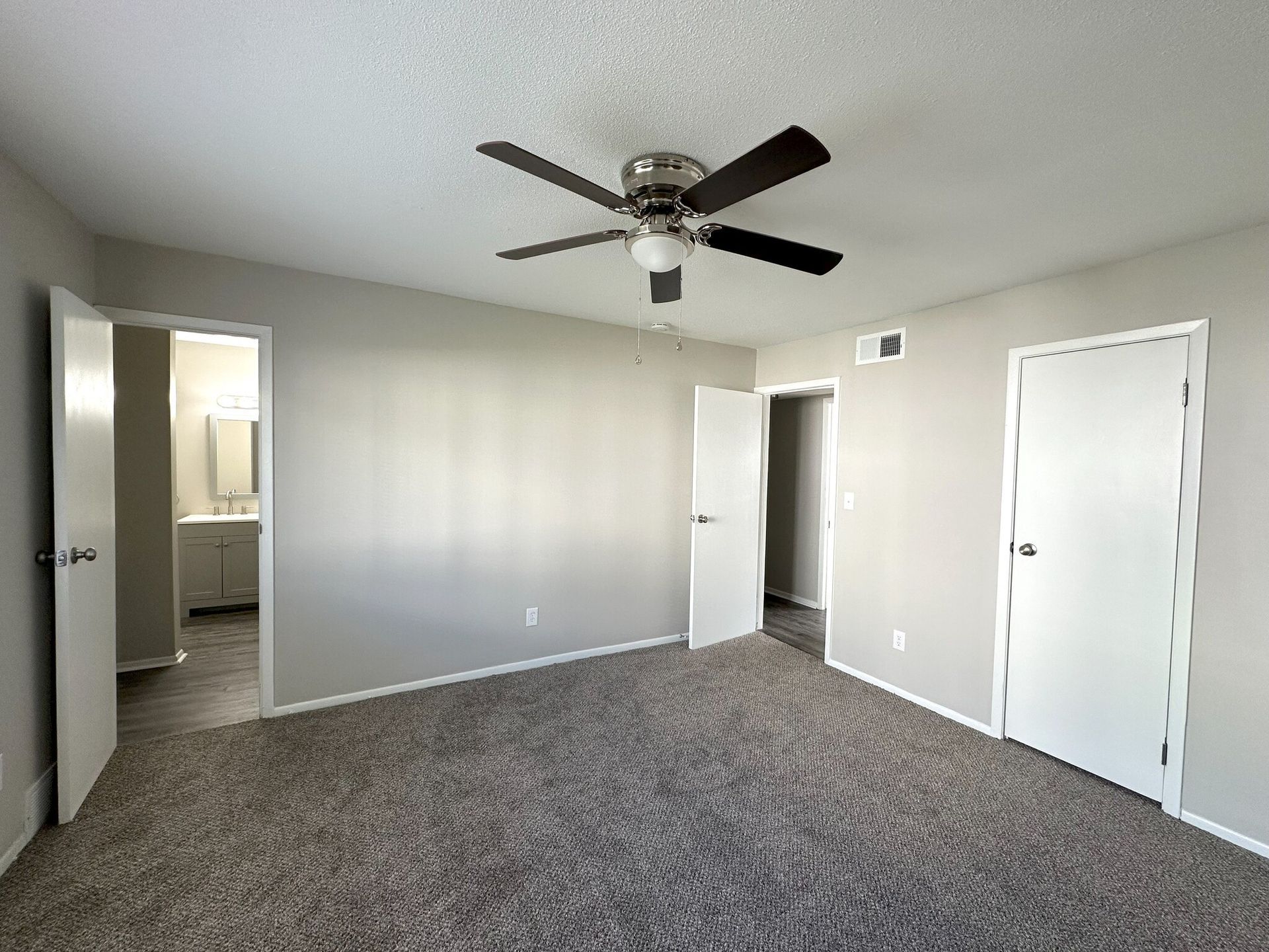 An empty bedroom with a ceiling fan and a bathroom.