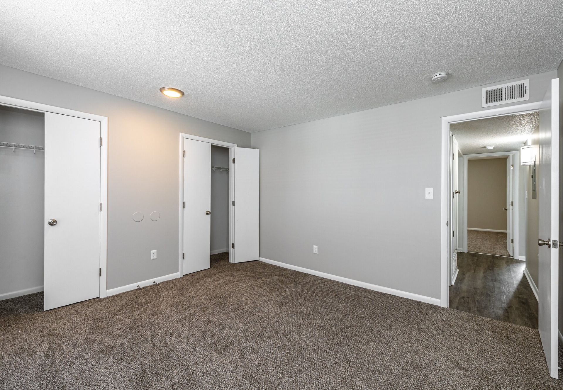 An empty bedroom with a carpeted floor and white doors.
