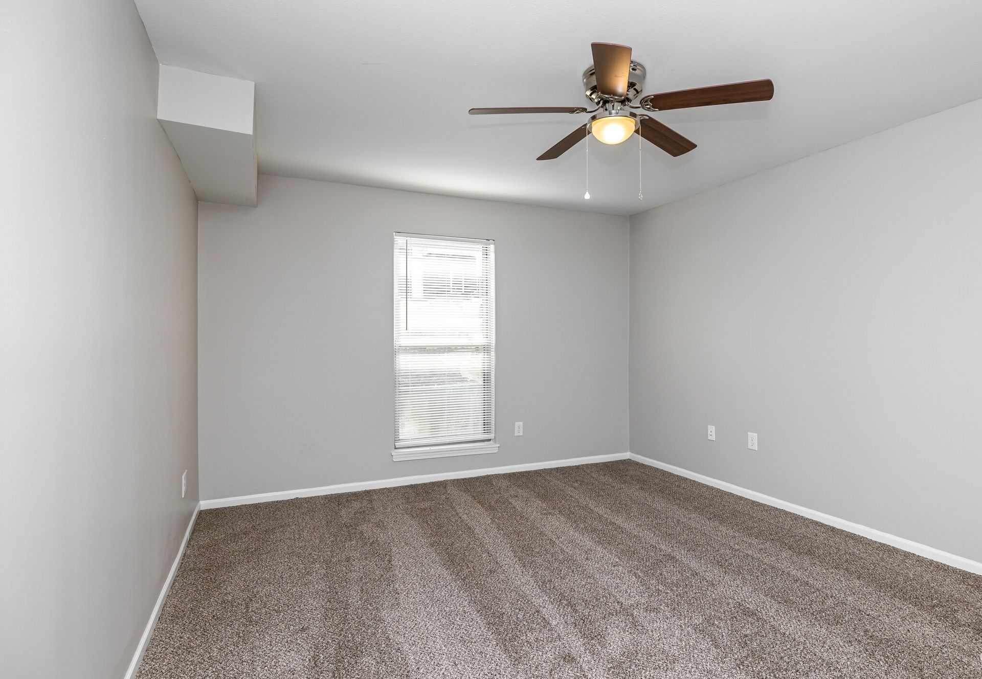 An empty bedroom with a ceiling fan and a window.