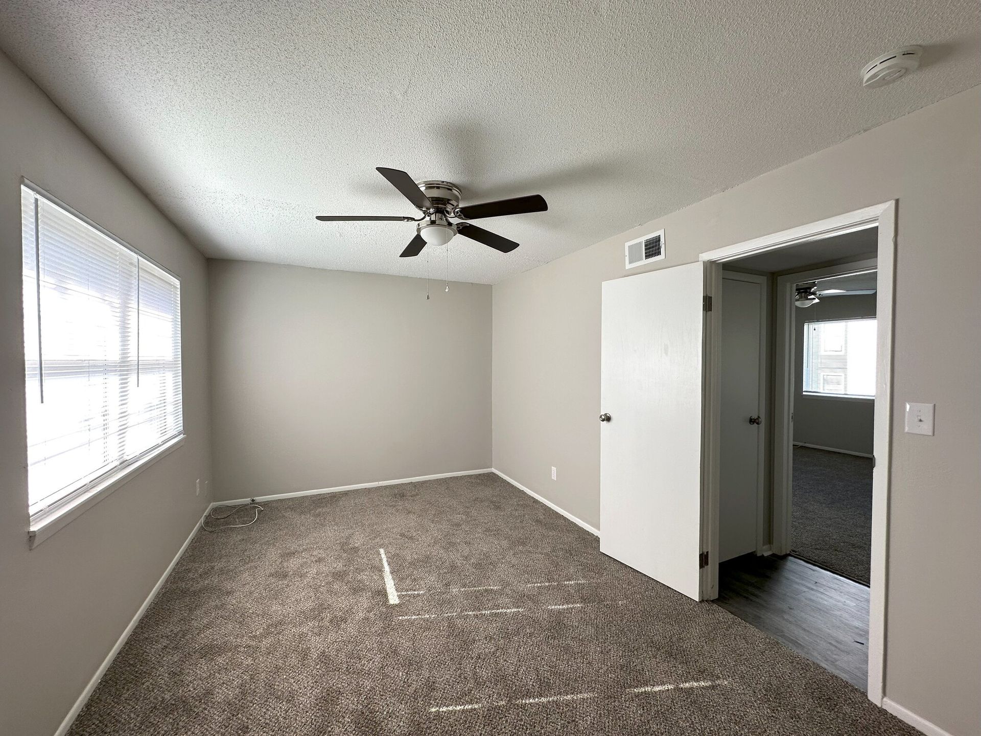 An empty bedroom with a ceiling fan and two windows.