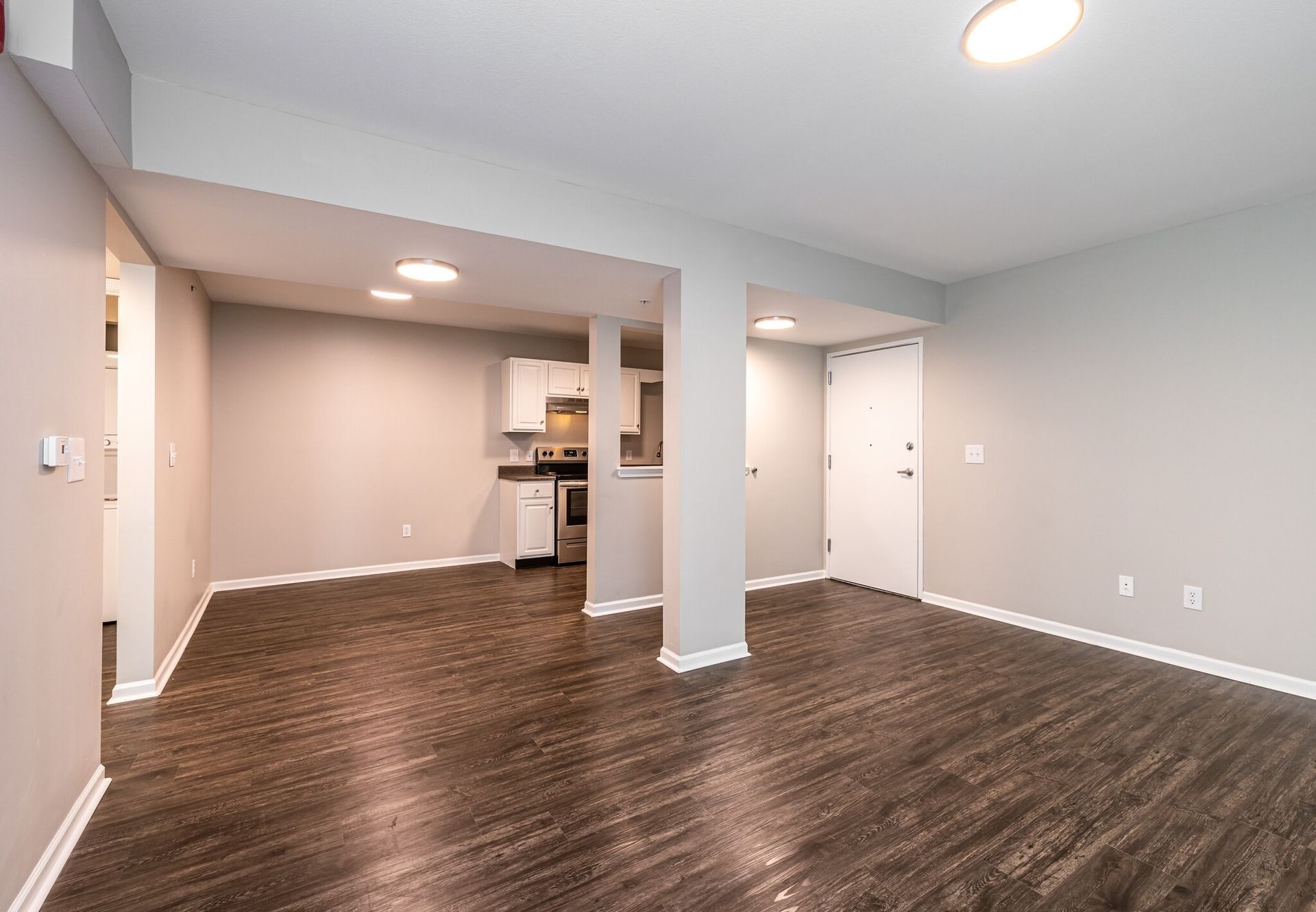 An empty living room with hardwood floors and a kitchen in the background.
