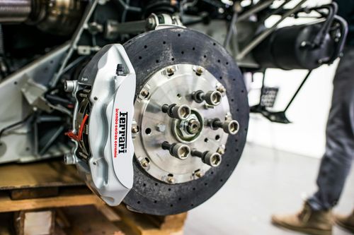 A high-performance Ferrari brake caliper and drilled carbon-ceramic disc rotor attached to a vehicle suspension system.