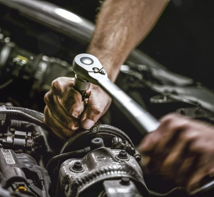 A close-up view of hands using a ratchet wrench to tighten a bolt on a car engine in a dimly lit garage.