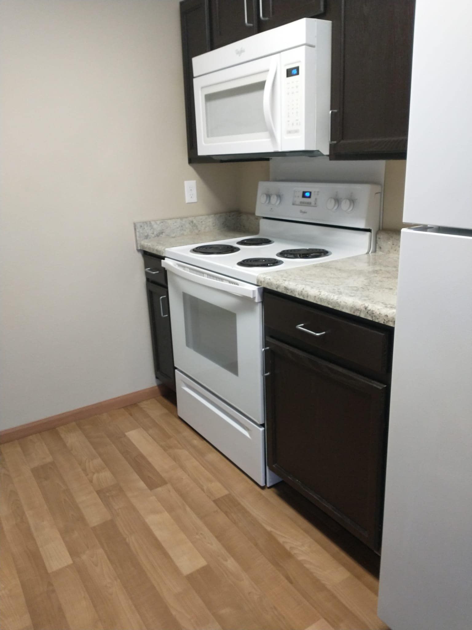 Kitchen with white stove, microwave, cabinets, and light countertop. Wooden floor.