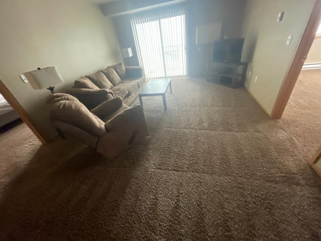 Living room with brown sectional sofa, sliding glass door, and brown carpet.
