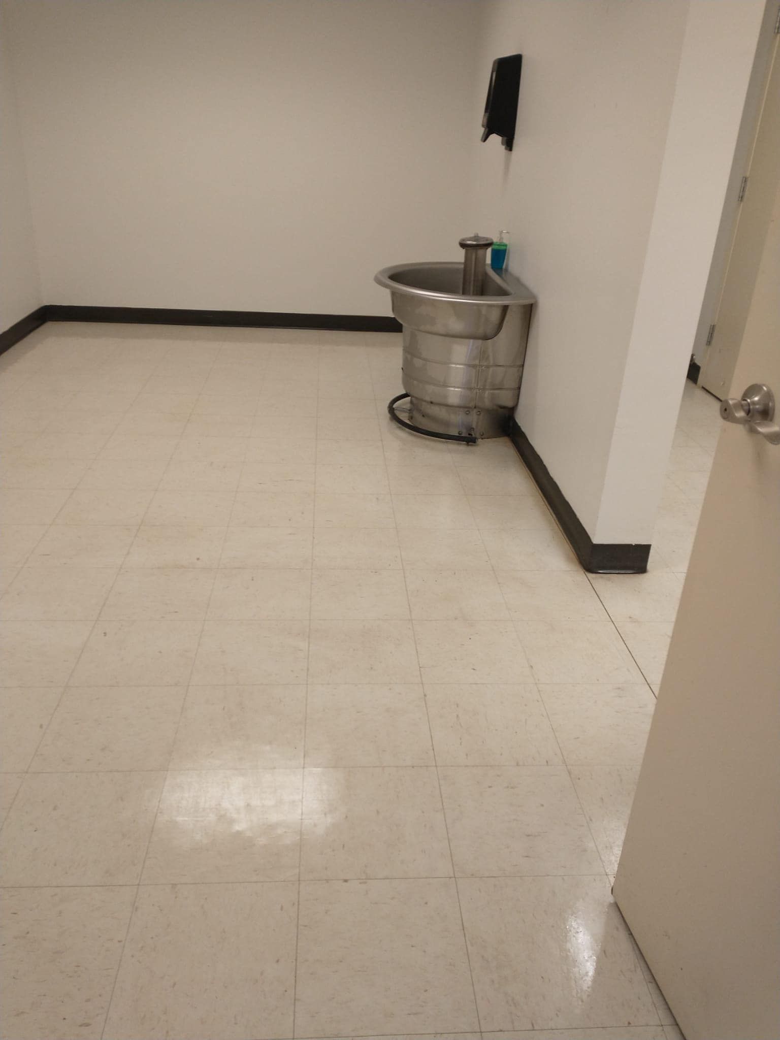 Empty room with a large stainless steel sink, white walls, and light-colored tiled floor.