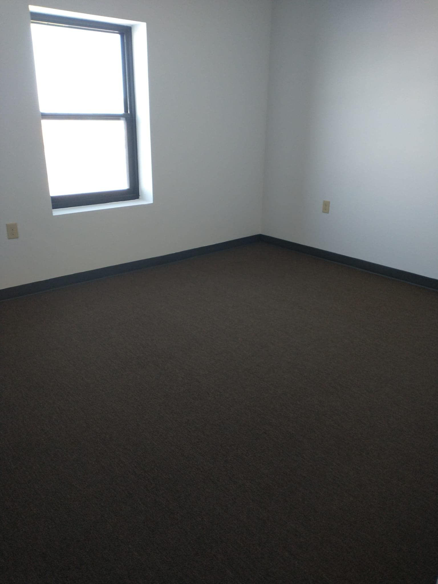 Empty room with brown carpet, white walls, and a window.