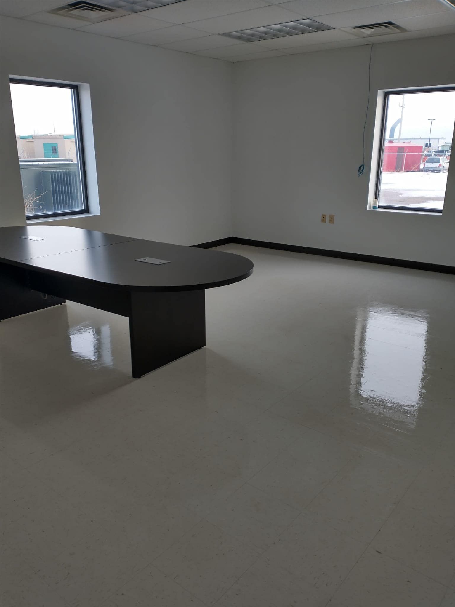 Empty office space with glossy, light-colored floor, two windows, and dark oval table.