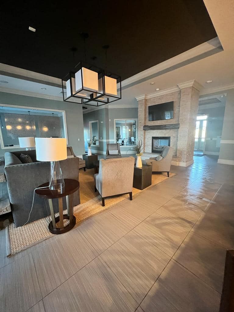 Lounge area with gray sofas, armchairs, fireplace, and chandelier. Light hardwood floors and a dark ceiling.