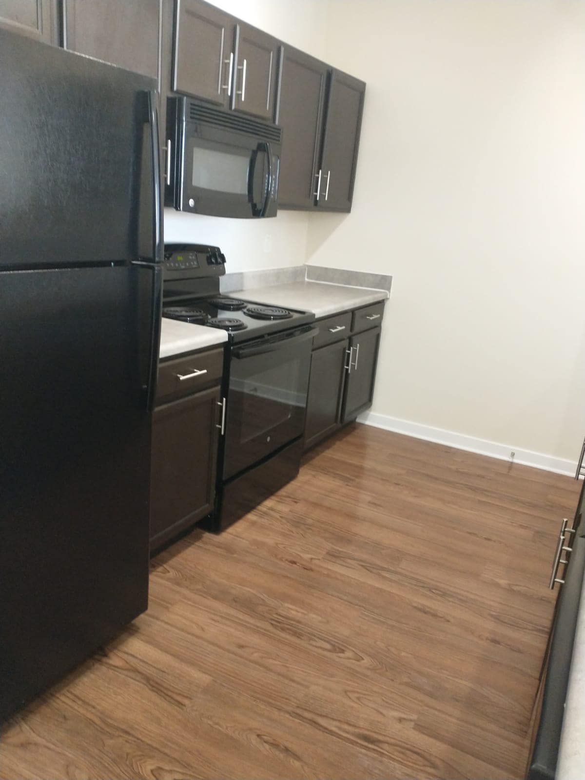 Kitchen with dark brown cabinets, black appliances, light countertop, and wood-look flooring.