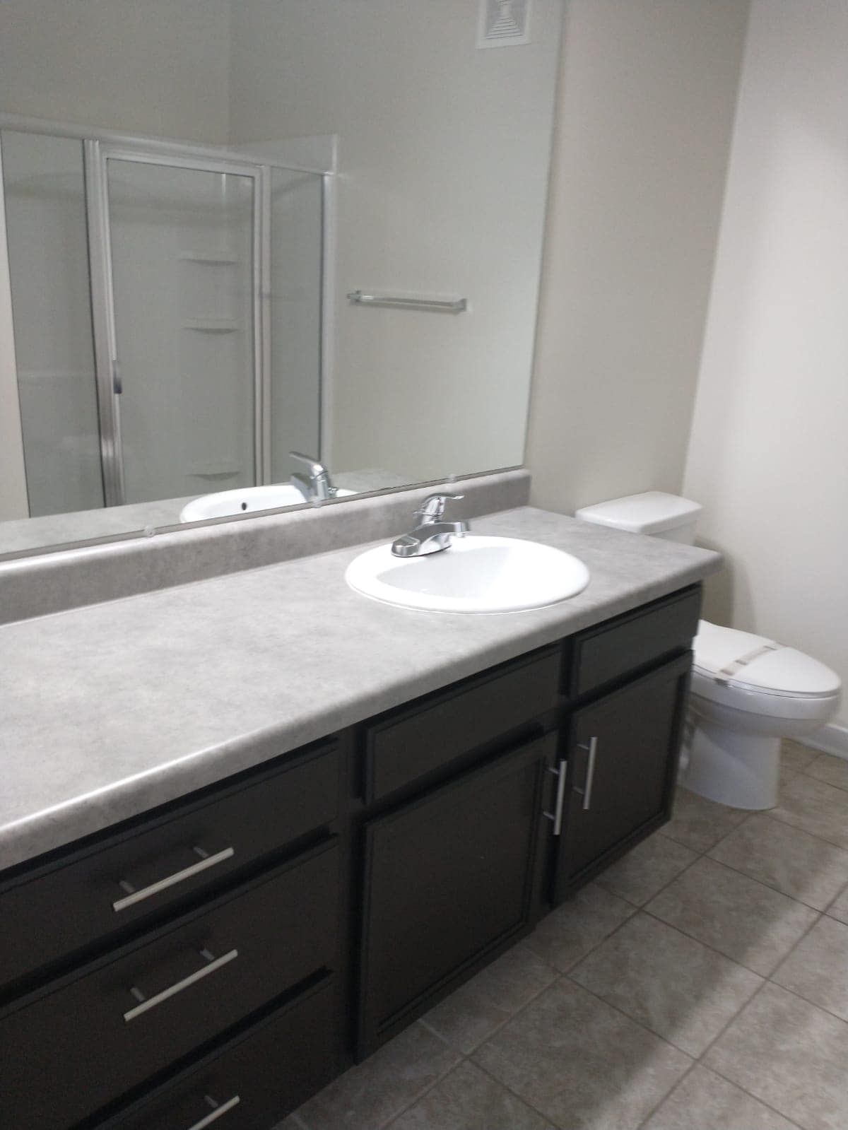 Bathroom with dark brown vanity, gray countertop, and white sink, toilet, and shower.