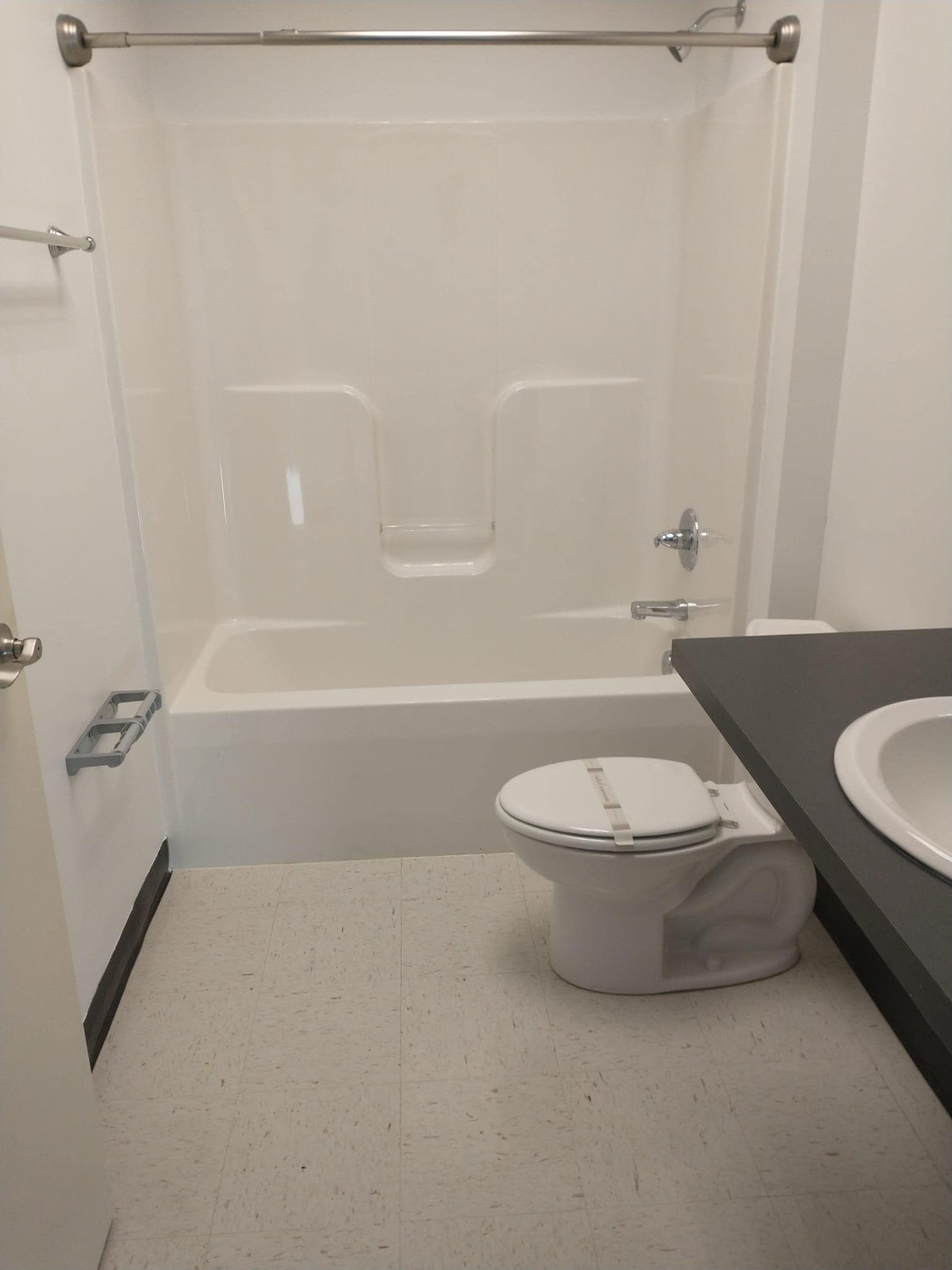 Bathroom with white bathtub, toilet, and sink; grey countertop, light floor.